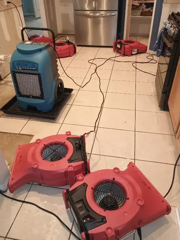 Red air movers and a dehumidifier on a tiled kitchen floor