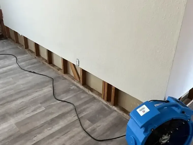 Blue air mover beside an opened wall base and stripped flooring